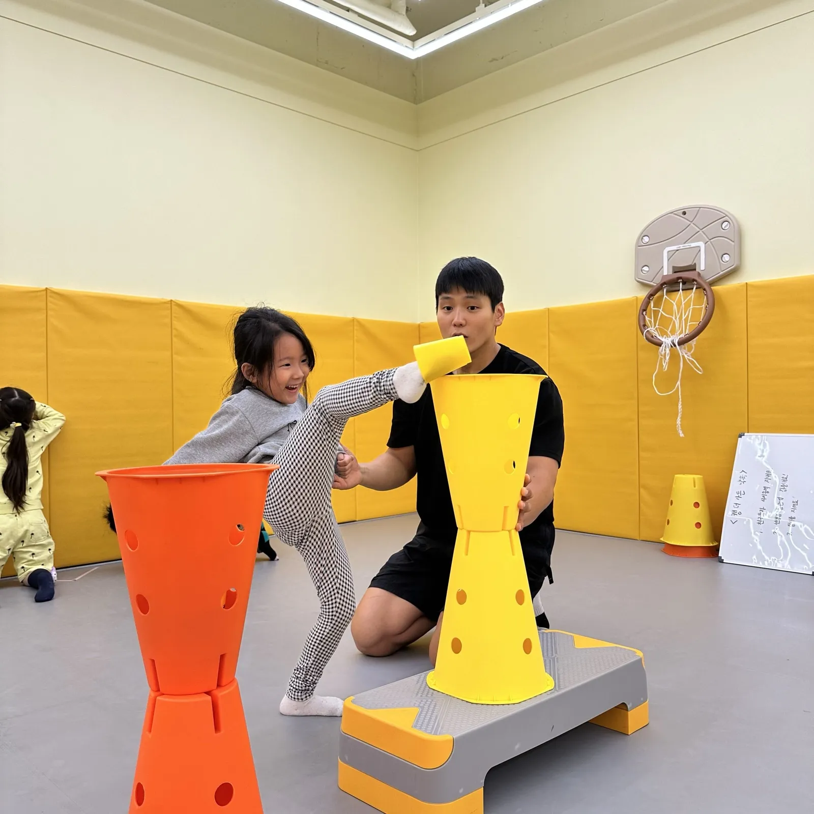 선생님이 잡아 준 콘 위의 컵을 발로 차 보는 아이