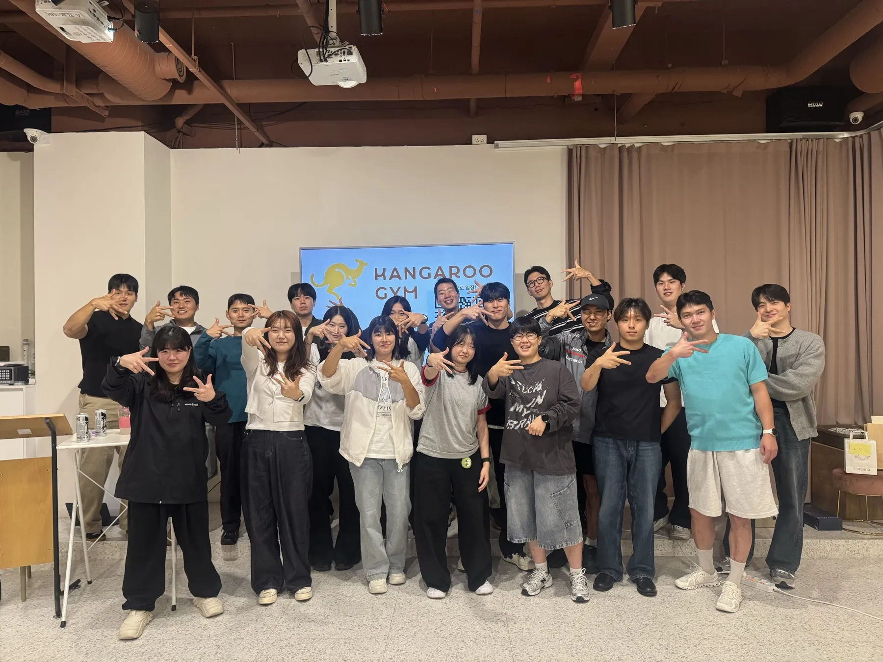 캥거루짐 로고 화면 앞에 모여 함께 손 포즈를 취한 선생님들